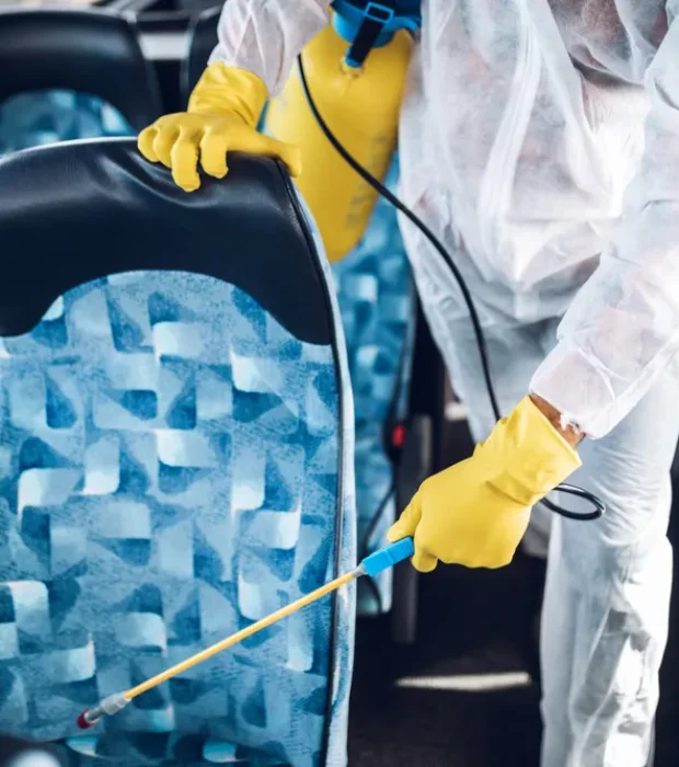 Technician wearing protective gear disinfecting bus seats in Melbourne, showcasing effective Transport Pest Solutions for public transportation.